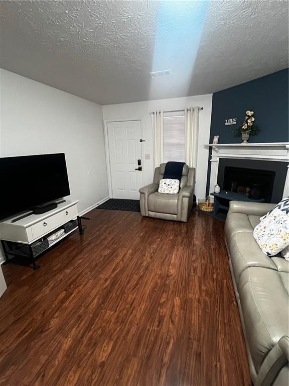 living room featuring visible vents, a textured ceiling, a fireplace with raised hearth, and wood finished floors