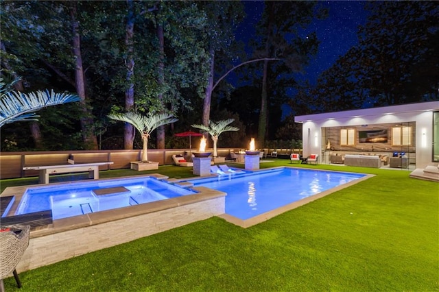 pool at night with an outbuilding, a fire pit, and a lawn