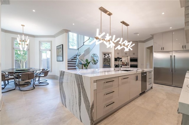 kitchen with light stone countertops, sink, hanging light fixtures, stainless steel appliances, and a center island with sink