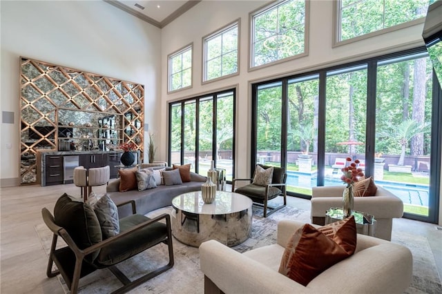 living room with a healthy amount of sunlight, crown molding, a high ceiling, and bar area