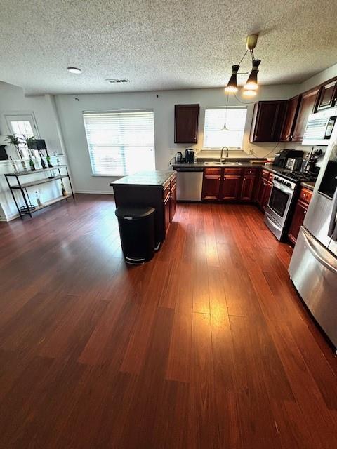 7178 Glaspie Way, Atlanta, GA 30349 - kitchen featuring stainless steel appliances, a textured ceiling, healthy amount of natural light, dark wood-style flooring, and pendant lighting
