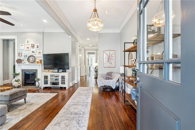 living room with ceiling fan, crown molding, a tile fireplace, and dark wood-type flooring