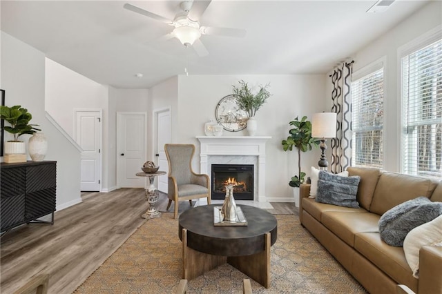 living area with ceiling fan, a fireplace, baseboards, and wood finished floors