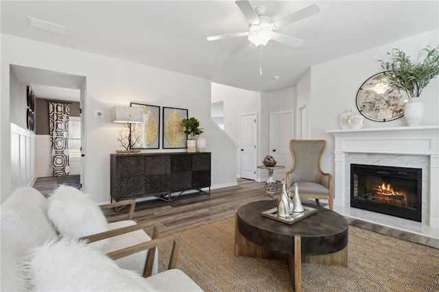 living room with visible vents, a premium fireplace, wood finished floors, and a ceiling fan