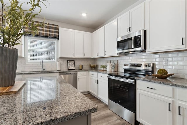 kitchen with stainless steel appliances, decorative backsplash, white cabinetry, a sink, and light wood-type flooring