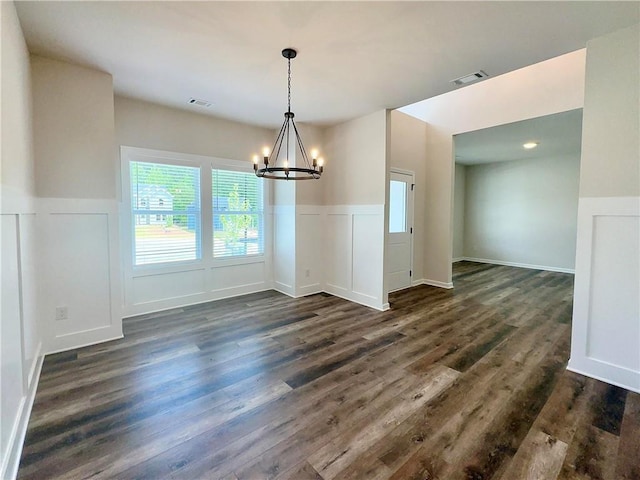 unfurnished dining area featuring dark wood-style flooring, visible vents, a wainscoted wall, and an inviting chandelier