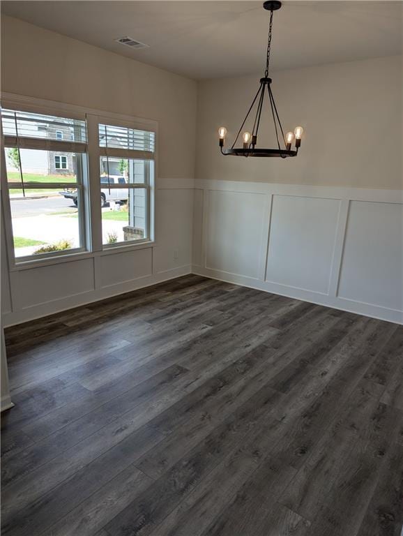 unfurnished dining area with a chandelier, a decorative wall, dark wood finished floors, and a healthy amount of sunlight