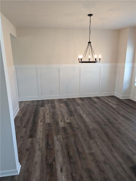 unfurnished dining area featuring a chandelier, wainscoting, and dark wood finished floors