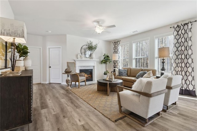 living area featuring visible vents, a premium fireplace, light wood-style flooring, and a ceiling fan