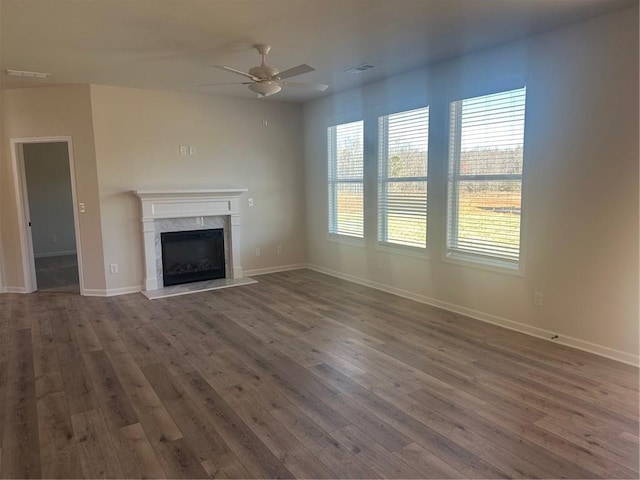 unfurnished living room featuring wood finished floors, a ceiling fan, baseboards, visible vents, and a high end fireplace