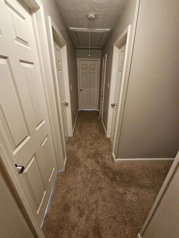 hall featuring dark carpet and a textured ceiling