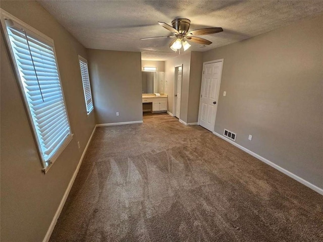 unfurnished bedroom featuring ceiling fan, carpet floors, a textured ceiling, and connected bathroom