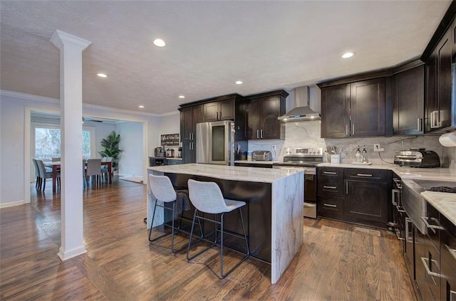 kitchen with a kitchen island, light stone countertops, stainless steel appliances, wall chimney range hood, and backsplash