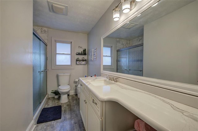 bathroom with toilet, wood finished floors, vanity, baseboards, and an enclosed shower