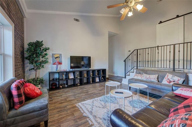 living area with wood finished floors, visible vents, crown molding, and a barn door