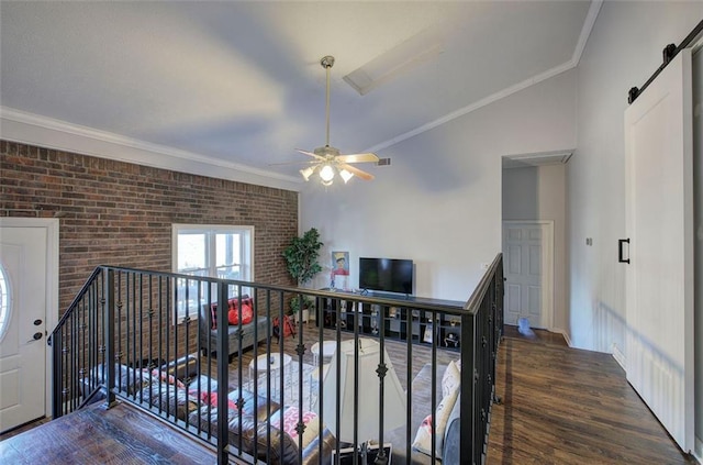 hall with dark wood finished floors, a barn door, ornamental molding, brick wall, and an upstairs landing