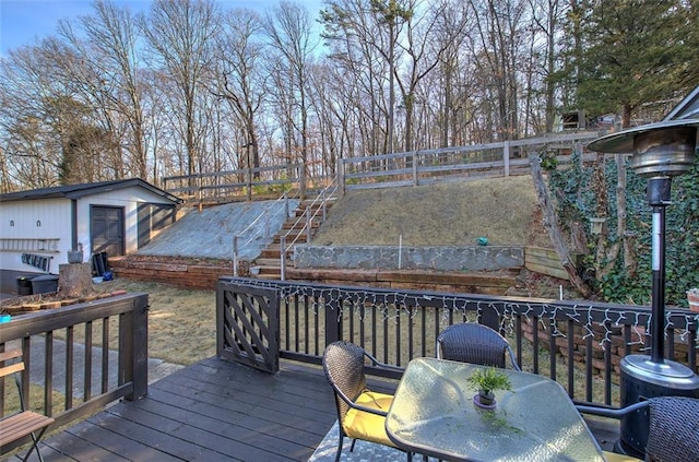 wooden terrace with stairway, fence, outdoor dining area, and an outbuilding