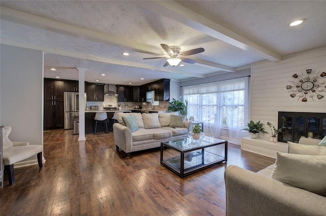 living area with a textured ceiling, a large fireplace, dark wood finished floors, and beam ceiling