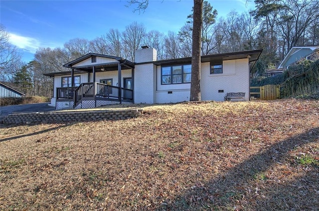 rear view of house with a deck, crawl space, brick siding, and a chimney