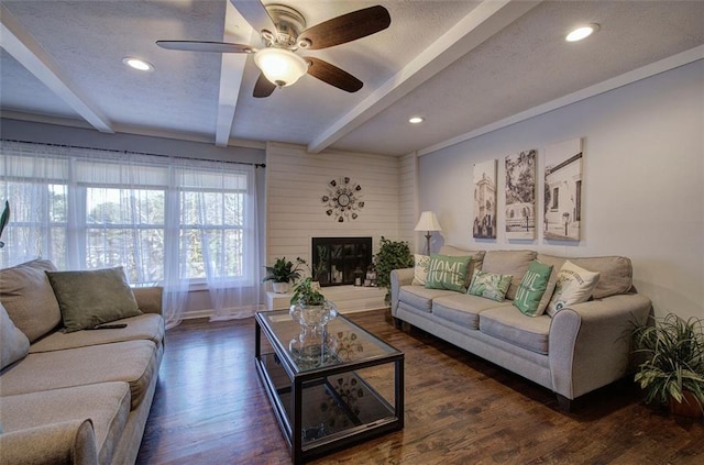 living area featuring dark wood-style flooring, a fireplace, beamed ceiling, and a textured ceiling