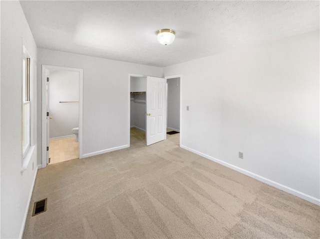 unfurnished bedroom featuring light carpet, ensuite bathroom, visible vents, and baseboards