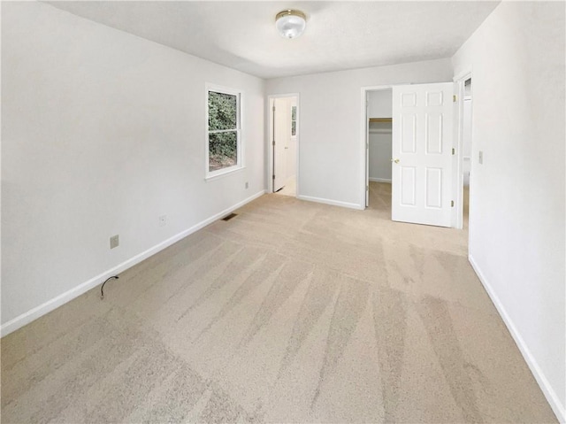 unfurnished bedroom with light carpet, visible vents, baseboards, a closet, and a walk in closet