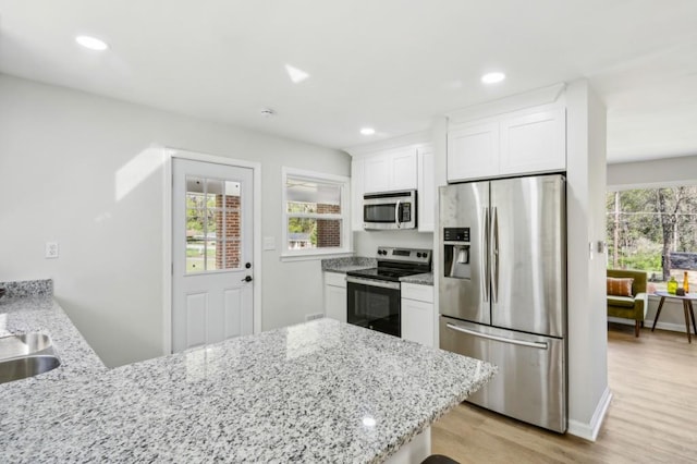 2519 Miriam Ln, Decatur, GA 30032 - kitchen with a peninsula, light wood finished floors, light stone countertops, appliances with stainless steel finishes, and white cabinetry
