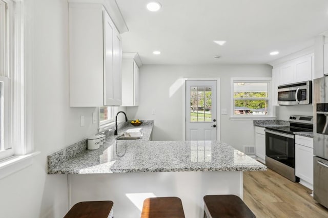 2519 Miriam Ln, Decatur, GA 30032 - kitchen featuring a breakfast bar area, a sink, white cabinets, a peninsula, and appliances with stainless steel finishes