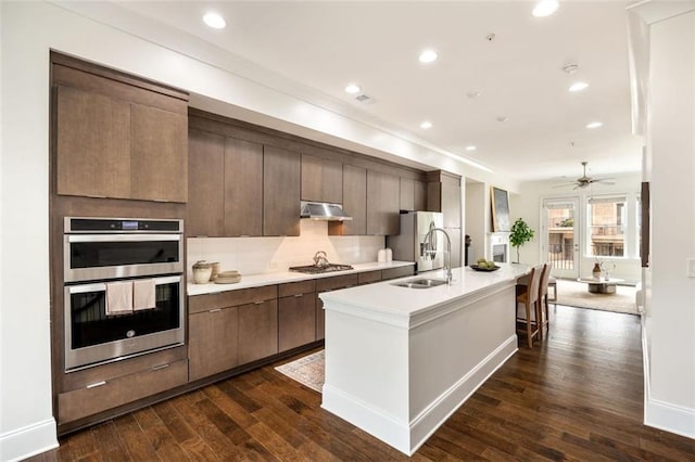 kitchen with an island with sink, stainless steel appliances, dark wood-type flooring, and sink