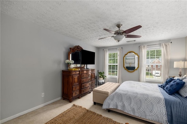bedroom featuring light carpet, multiple windows, baseboards, a textured ceiling, and ceiling fan