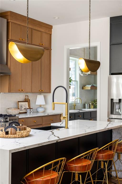 kitchen with tasteful backsplash, wall chimney range hood, a breakfast bar, sink, and light stone counters