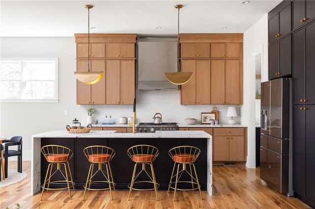 kitchen with ventilation hood, a center island with sink, hanging light fixtures, and a breakfast bar area