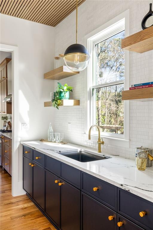 kitchen featuring light stone countertops, light hardwood / wood-style floors, sink, stainless steel stove, and backsplash