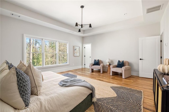 bedroom featuring a raised ceiling, wood-type flooring, and an inviting chandelier