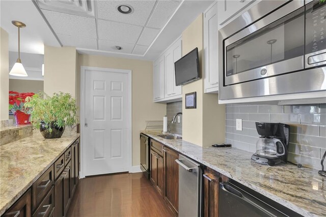 kitchen with appliances with stainless steel finishes, dark wood-type flooring, dark brown cabinetry, pendant lighting, and white cabinetry