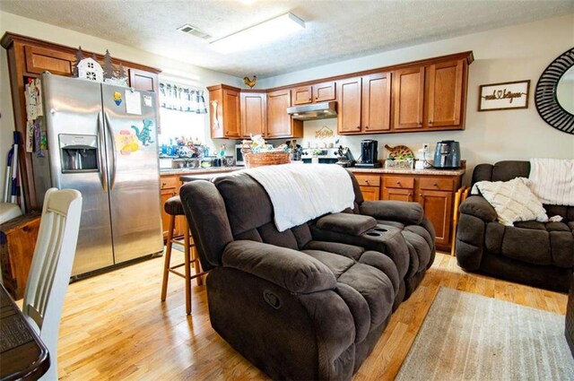 kitchen with stainless steel fridge, light wood-style floors, open floor plan, light countertops, and under cabinet range hood