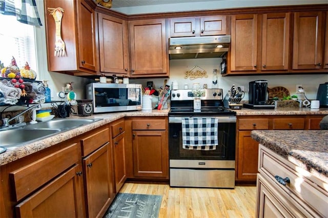 kitchen with under cabinet range hood, stainless steel appliances, a sink, light wood finished floors, and brown cabinetry