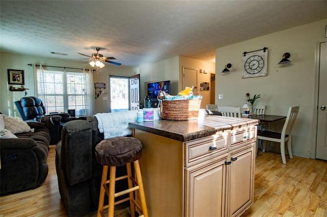 kitchen featuring visible vents, light wood-style flooring, a breakfast bar area, open floor plan, and a textured ceiling