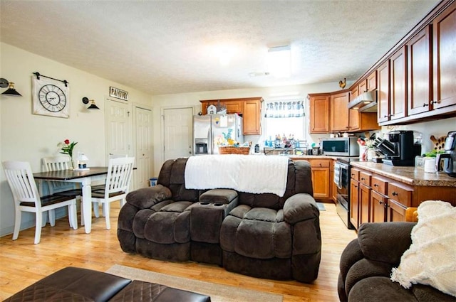 kitchen with under cabinet range hood, stainless steel appliances, light wood-style floors, and open floor plan