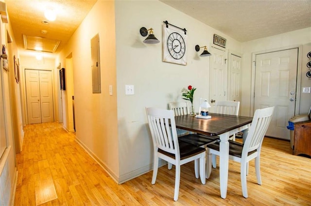 dining room with light wood-style floors, electric panel, a textured ceiling, and baseboards