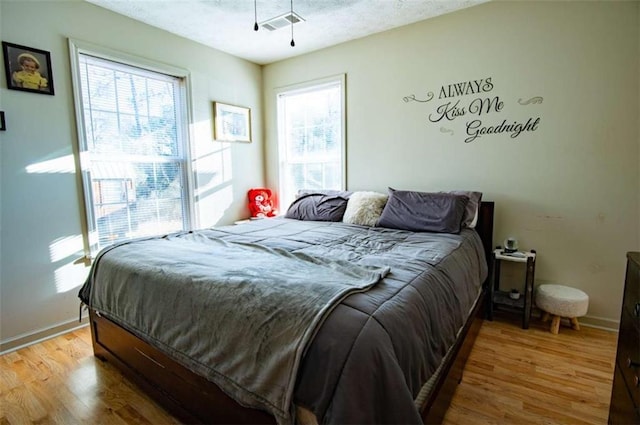 bedroom with a textured ceiling, wood finished floors, visible vents, and baseboards