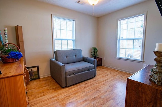 living area featuring light wood finished floors, a ceiling fan, visible vents, and baseboards