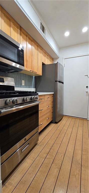kitchen with appliances with stainless steel finishes, light wood-style floors, light countertops, light brown cabinetry, and backsplash