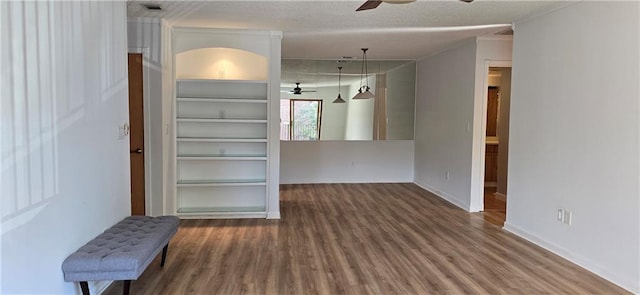 empty room with ceiling fan, hardwood / wood-style flooring, built in shelves, and a textured ceiling