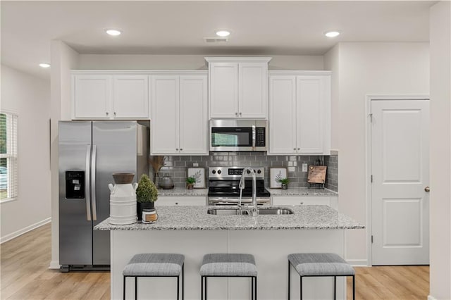 kitchen featuring stainless steel appliances, white cabinets, a sink, and light wood-style flooring