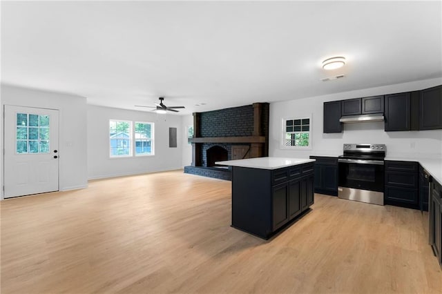 44 Crayton St, Rockmart, GA 30153 - kitchen featuring stainless steel electric range, dark cabinetry, under cabinet range hood, a brick fireplace, and light wood-style flooring