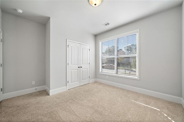 unfurnished bedroom with light colored carpet and a closet