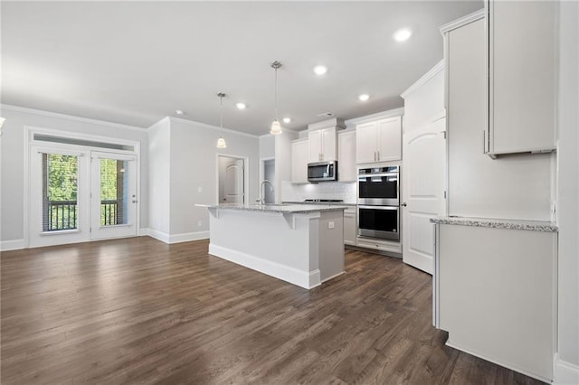 kitchen featuring appliances with stainless steel finishes, an island with sink, decorative light fixtures, white cabinets, and ornamental molding