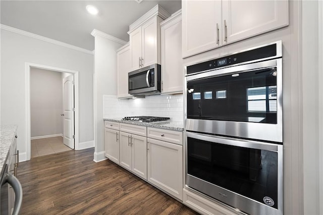 kitchen with white cabinets, dark hardwood / wood-style floors, appliances with stainless steel finishes, tasteful backsplash, and light stone counters