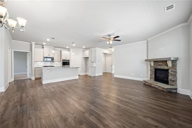 unfurnished living room with ceiling fan with notable chandelier, a stone fireplace, crown molding, and dark wood-type flooring